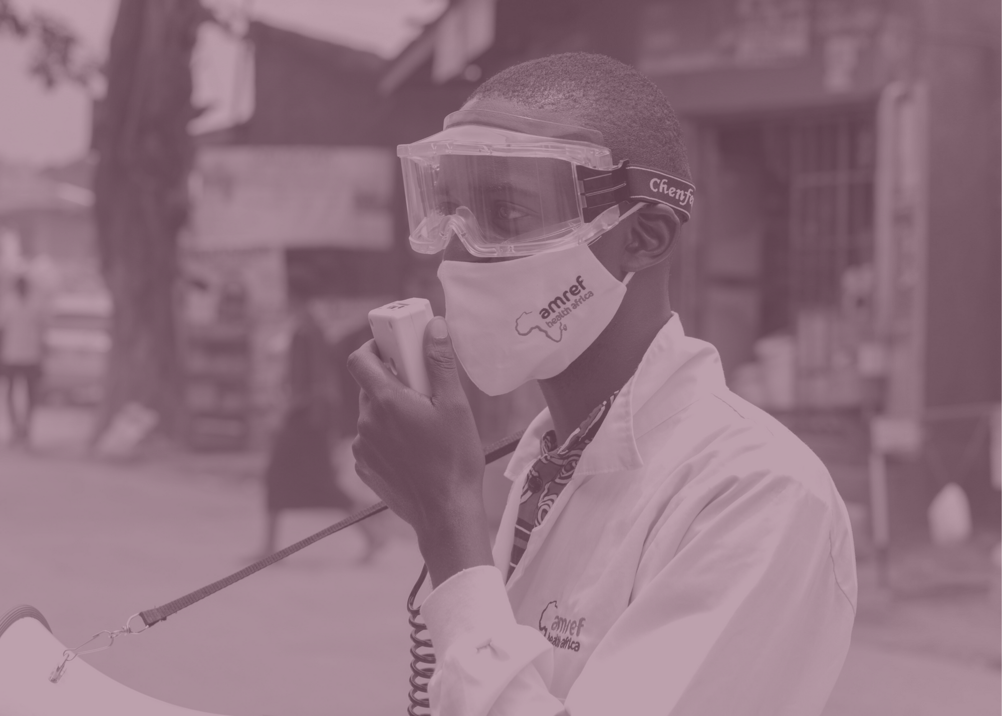 An Amref Healthworker with PPE speaking into a walkie talkie communicator.
