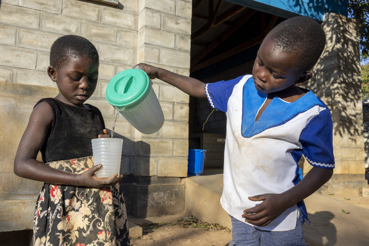 Five-year-old Frank pours water for his classmate Brenda