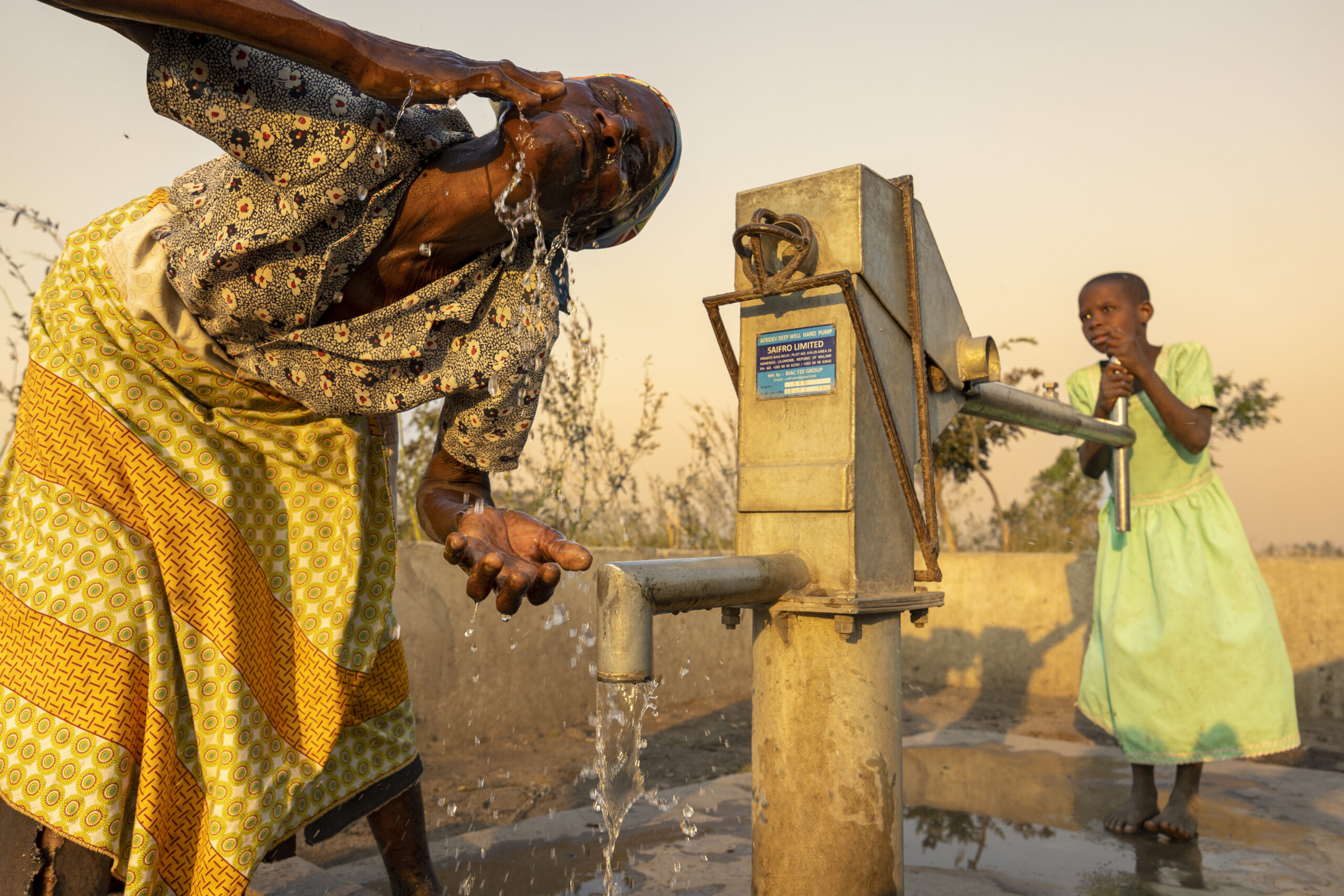 Elistina and her granddaughter Flora gathering water at the Amref borehole